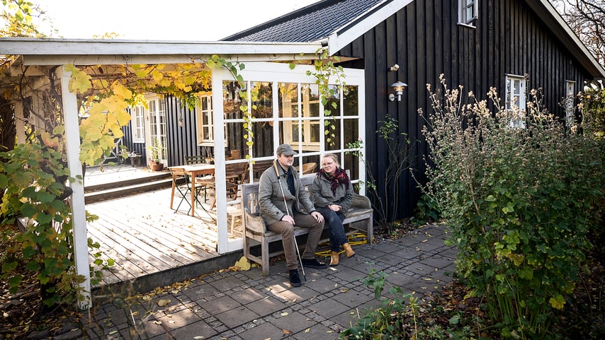 Par sidder på bænk foran hus