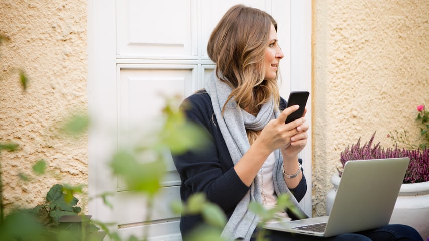 Kvinde sidder med telefon og computer