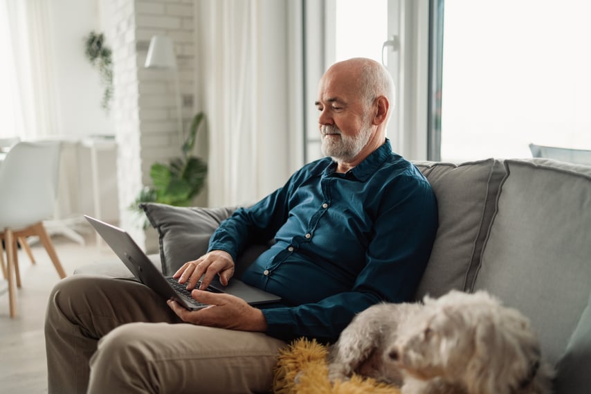 Ældre mand sidder på sofaen med computer